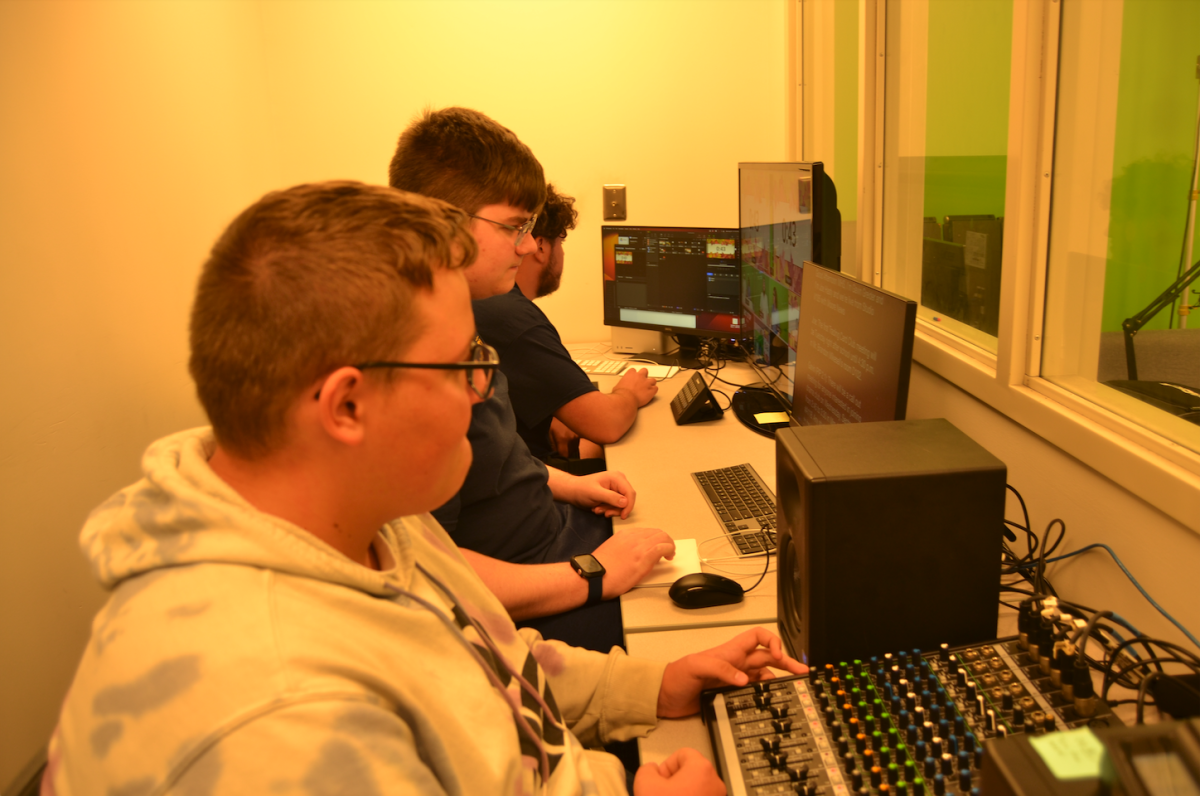 Jacob Pucket and Beau Mishler are preparing for a live broadcast. Pucket is as teleprompter while Mishler is seen handling audio. Mishler said," Audio can be tricky at times , but the feeling of completing a broadcast makes it well worth it."