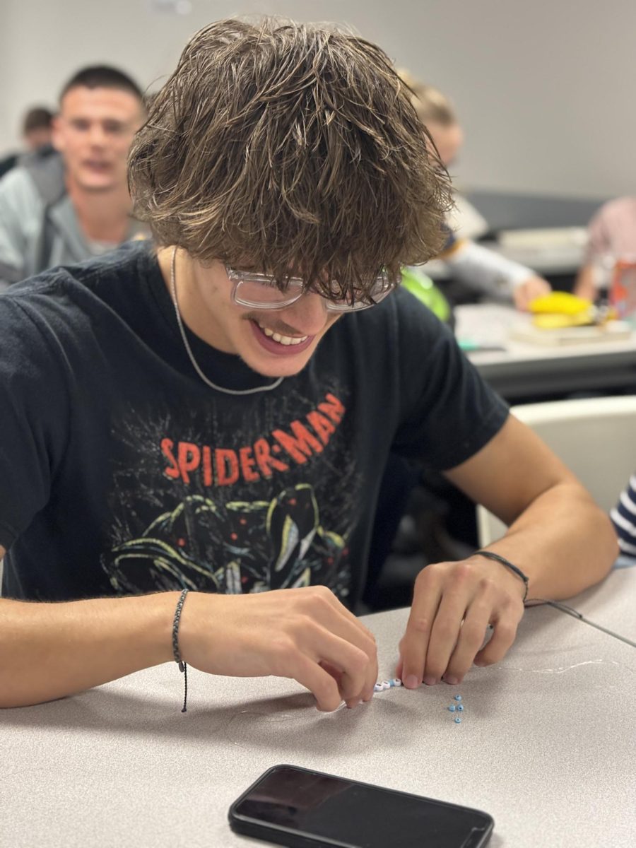 Senior Gage Carter laughs while making a bracelet with a bible verse on it during an FCA meeting.